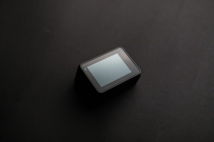 A sleek black action camera lies on a dark surface, showcasing its LCD screen.
