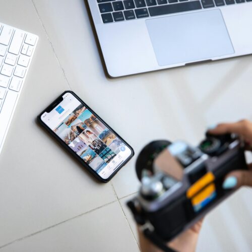 Person using vintage camera with smartphone and laptop in creative setup.