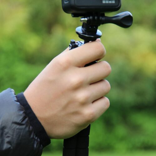 Close-up of a hand holding a GoPro camera on a tripod, ready for outdoor video recording.