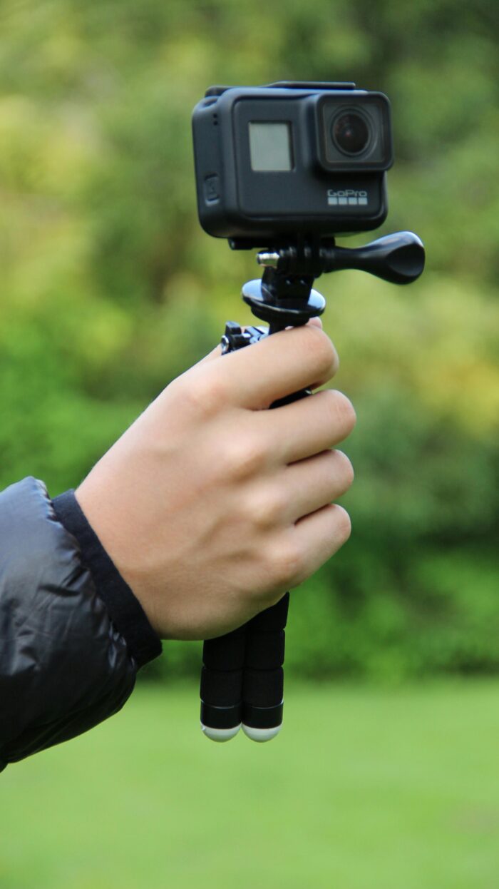Close-up of a hand holding a GoPro camera on a tripod, ready for outdoor video recording.